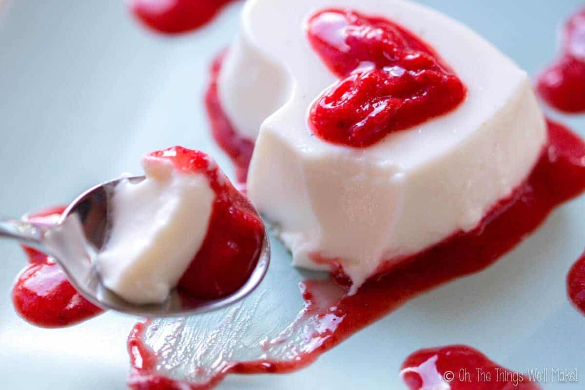 Scooping up a heart-shaped homemade panna cotta with strawberry puree on a spoon