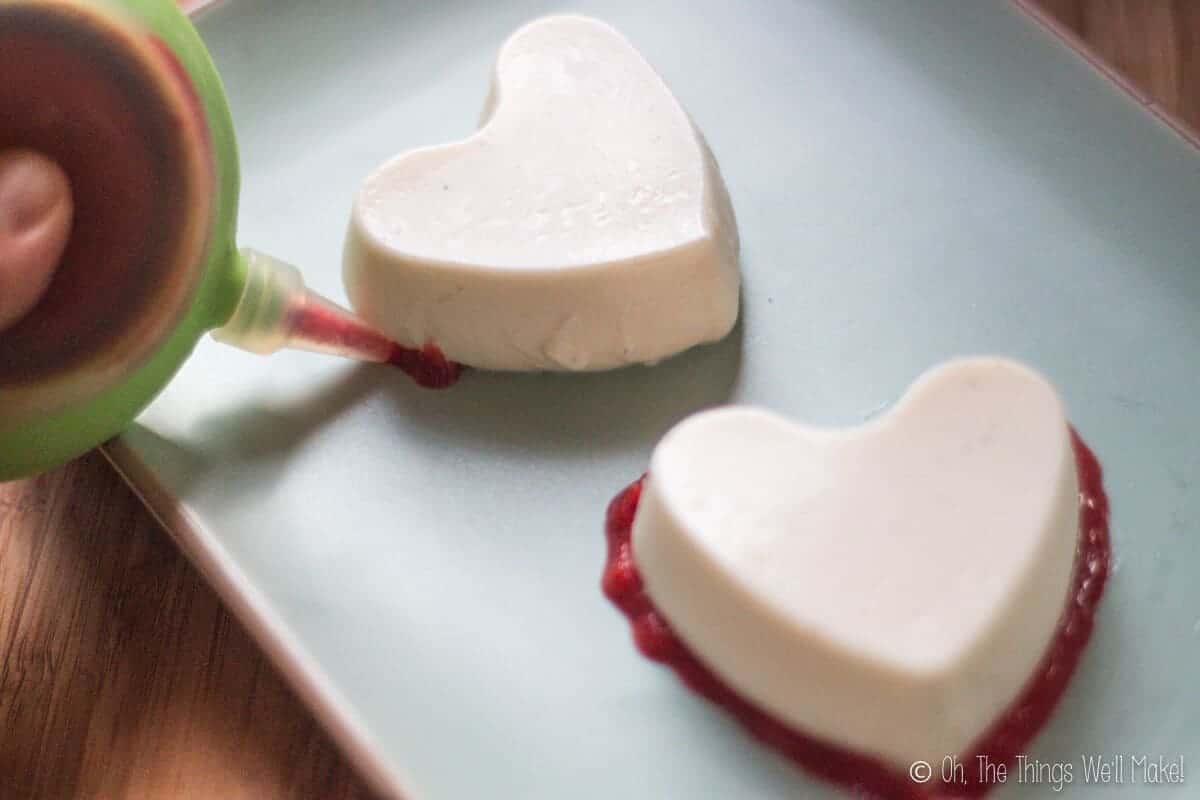 Decorating a homemade creamy panna cotta by piping a berry puree around the edges of the bottom.