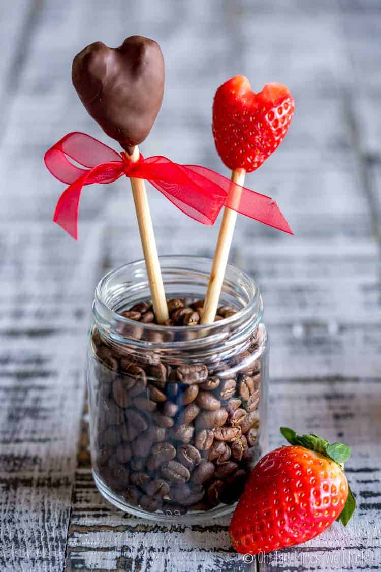 Several strawberry hearts on skewers, one covered in chocolate.
