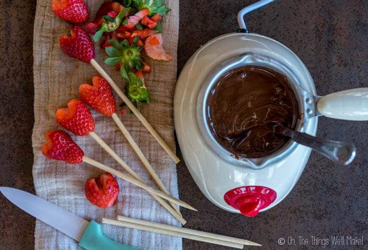 Overhead view of melted chocolate next to heart-shaped strawberries on sticks, ready to be dipped in the melted chocolate.