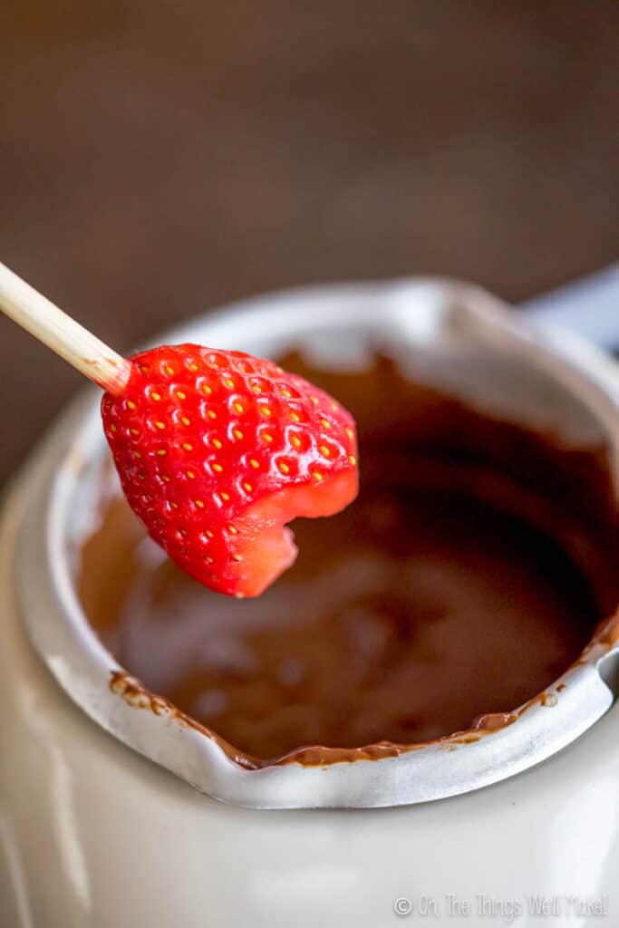 A heart shaped strawberry on a bamboo skewer, ready to be dipped into melted chocolate.