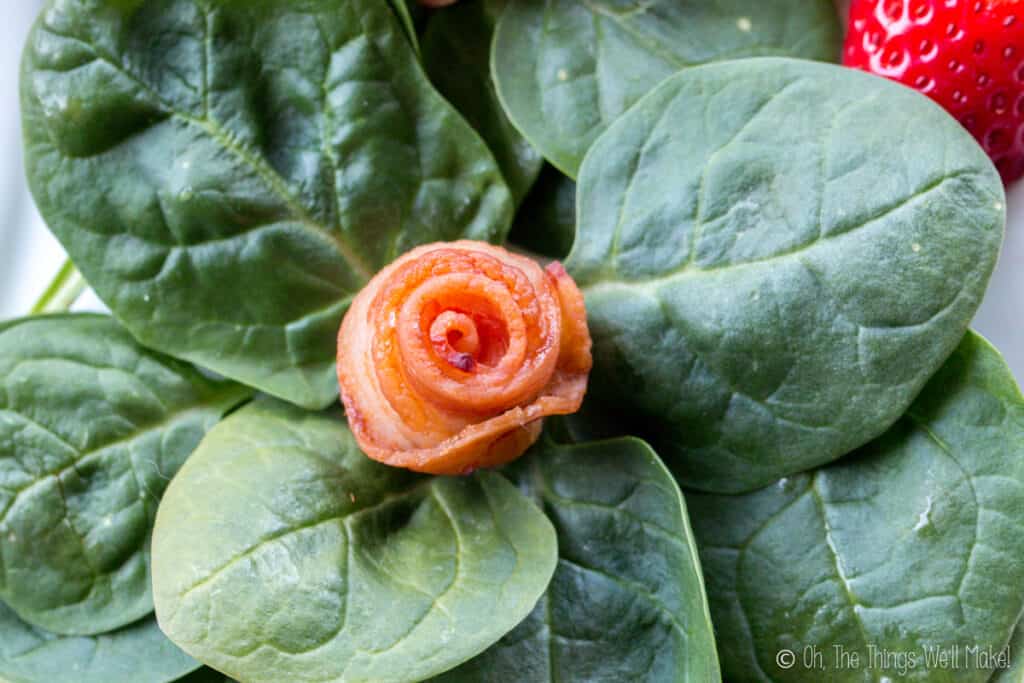 Placing a bacon rose on a nest of baby spinach leaves.