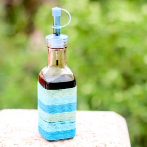 A clear glass bottle decorated with varying shades of blue string wrapped around it, filled with homemade balsamic reduction sauce.