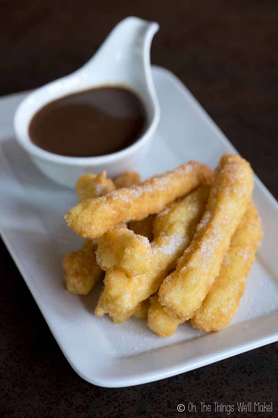 Overhead view of a plate of homemade grain free, gluten free churros with sugar sprinkled on top, next to a mug of Spanish hot chocolate