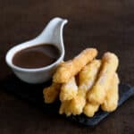 Grain-free, gluten-free churros on a slate platter accompanied by a cup of thick Spanish hot chocolate