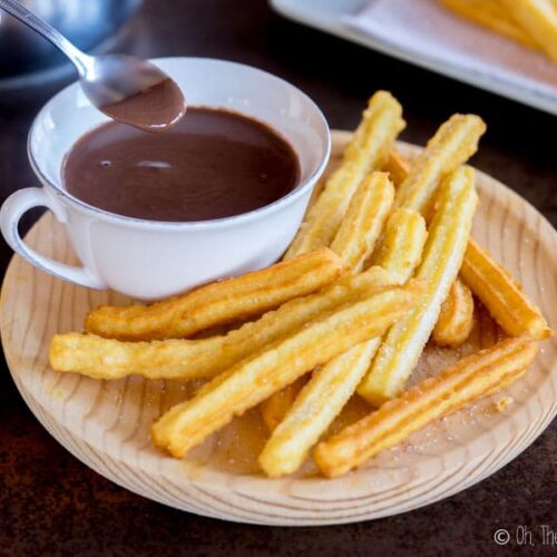 Overhead view of someone spooning up some Spanish hot chocolate from a platter with chocolate and churros.