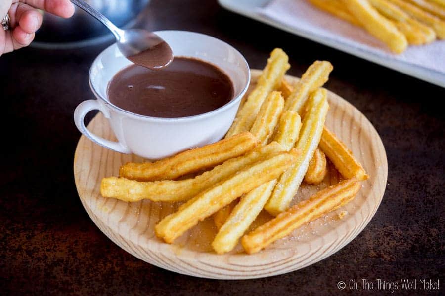 Overhead view of someone spooning up some Spanish hot chocolate from a platter with chocolate and churros.