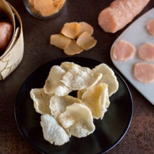 Crackers di gamberi fatti in casa su un piatto davanti a crackers di gamberi fatti in casa non cotti e un rotolo di pasta per crackers di gamberi.