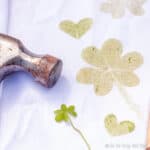 Closeup of a clover on a white cloth that has been covered with prints made by hammering clovers onto the cloth.