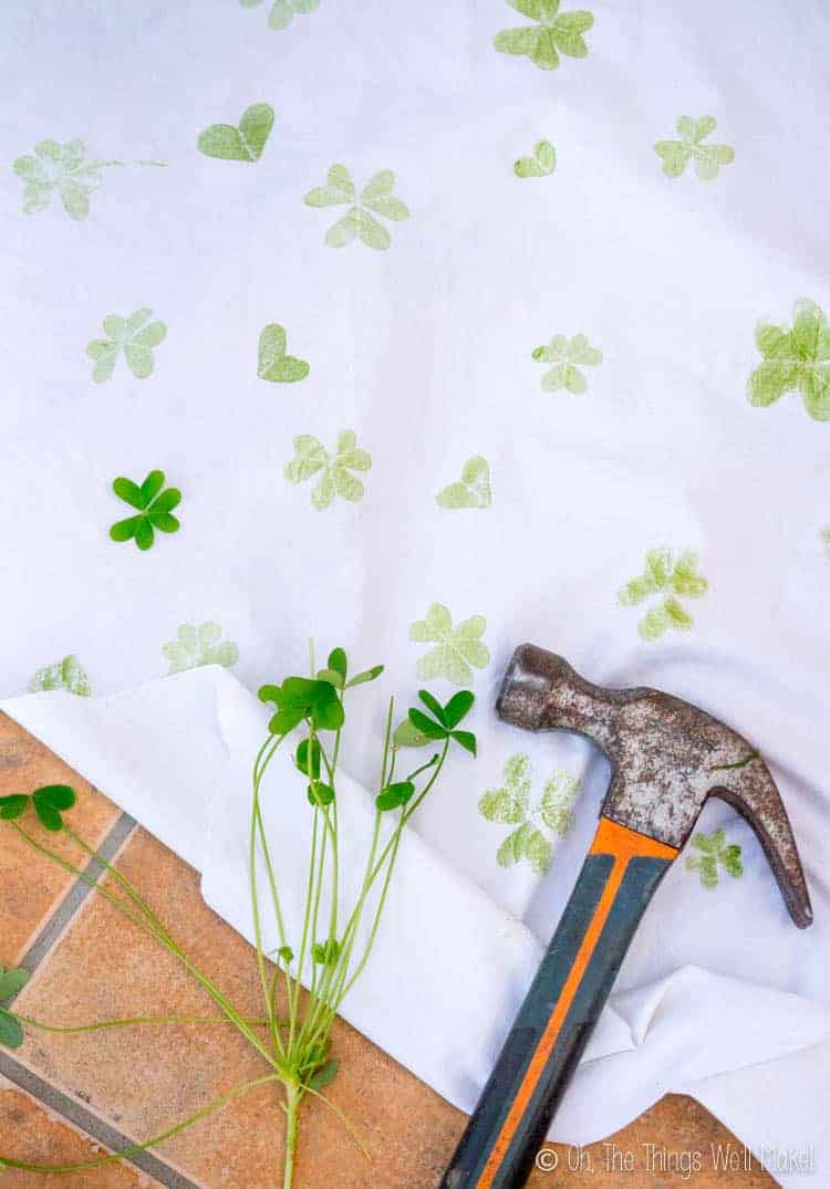 Overhead view of a hammer and clover leaves on a cloth with shamrock and clover heart prints on it.