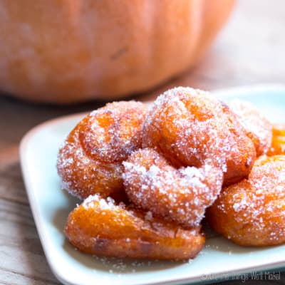 A closeup of a plate of pumpkin fritters covered with sugar.