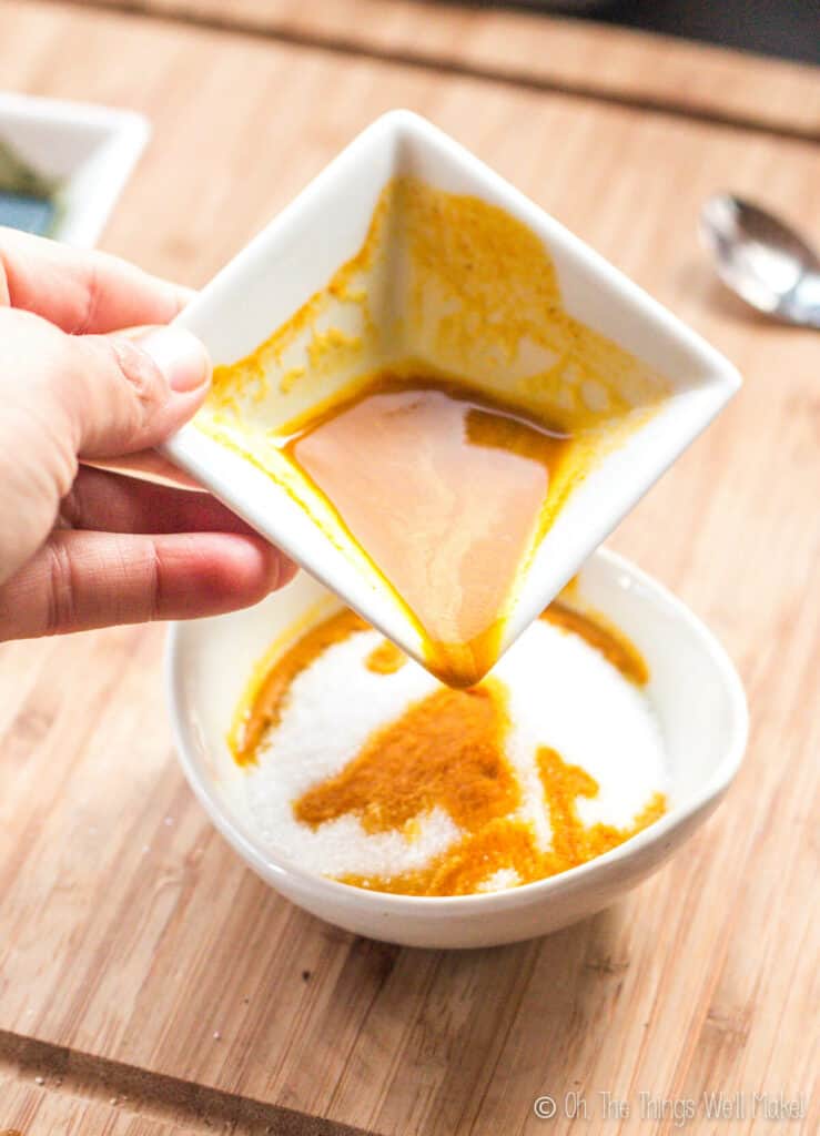 Pouring a mixture of turmeric and alcohol into a white bowl of sugar crystals