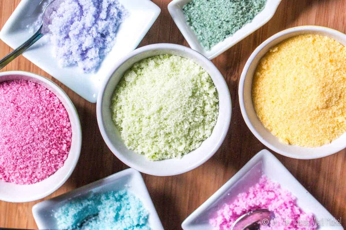 Overhead view of 7 small bowls filled with sugar that has been colored with a variety of homemade food colorings (in a variety of colors).