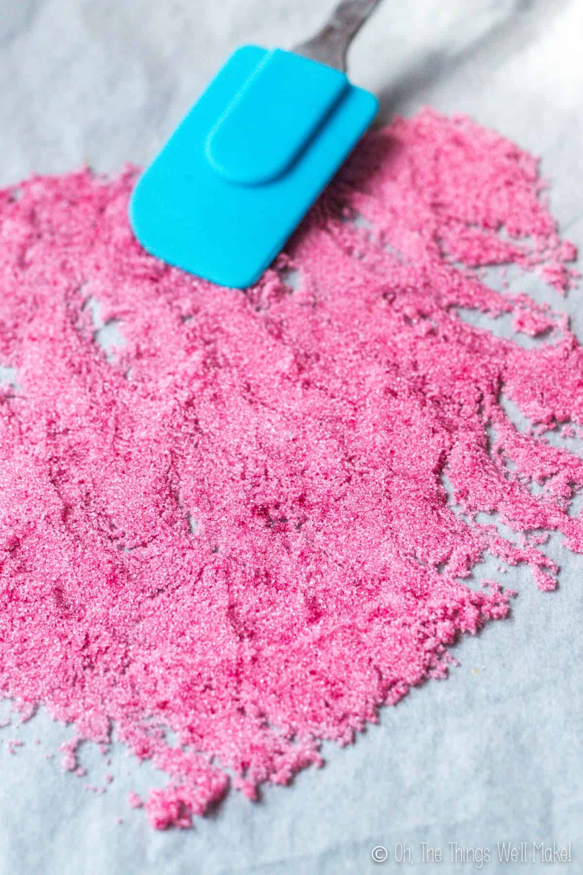 spreading pink sugar crystals over a parchment covered baking tray