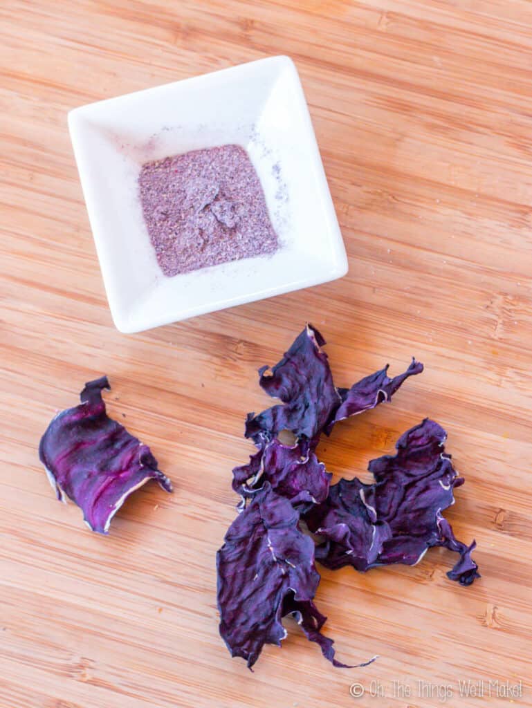 dried red cabbage leaves next to a bowl filled with a powder obtained from grinding the cabbage leaves.