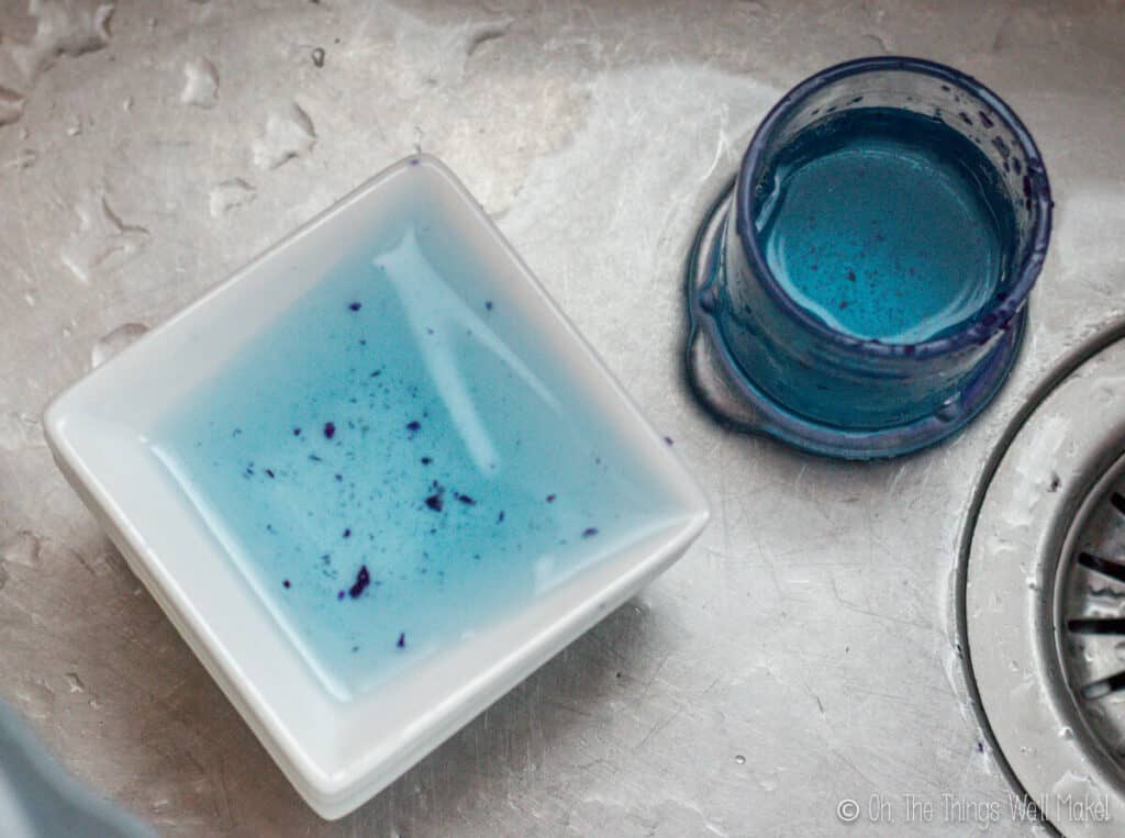 overhead view of blue liquid in a bowl and a glass in a sink with bits of red cabbage floating in the blue water.