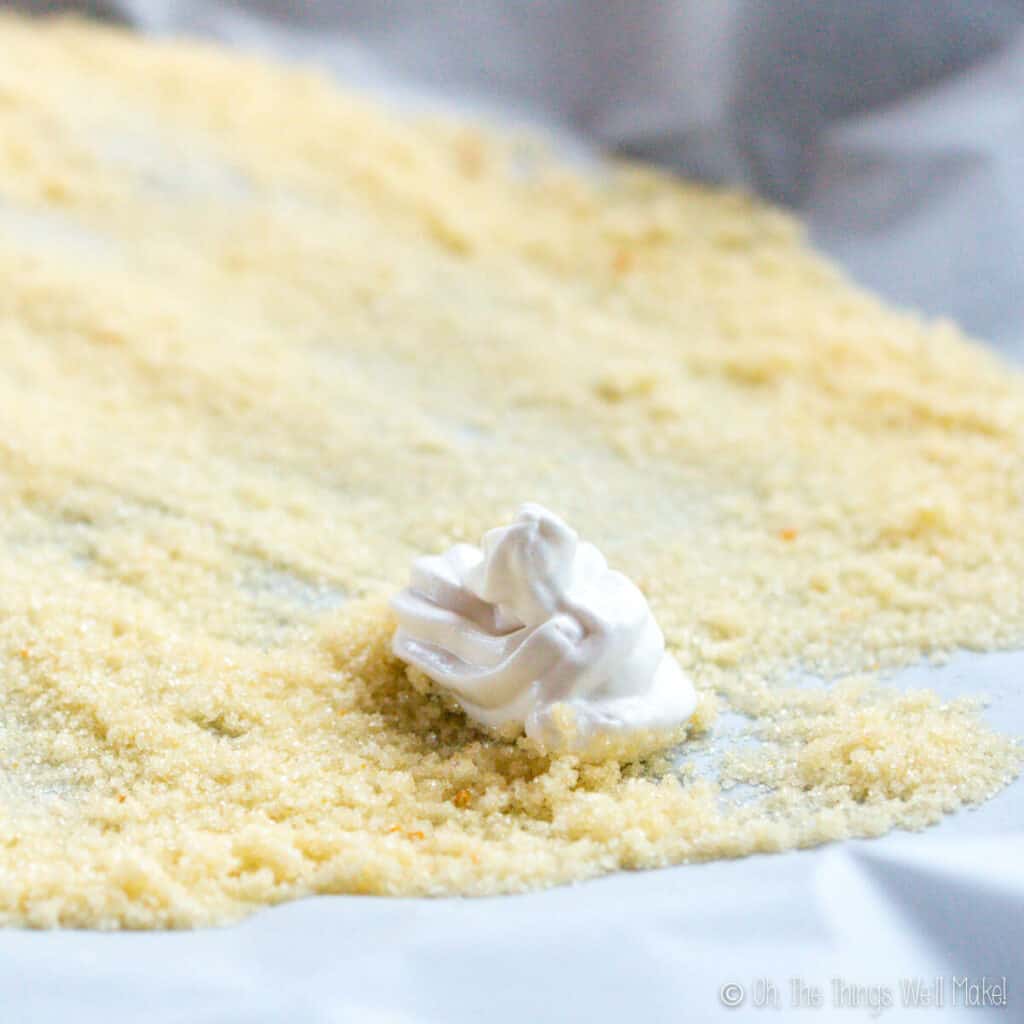 Making a piped marshmallow peep in the shape of a chick on top of yellow colored sugar crystals.