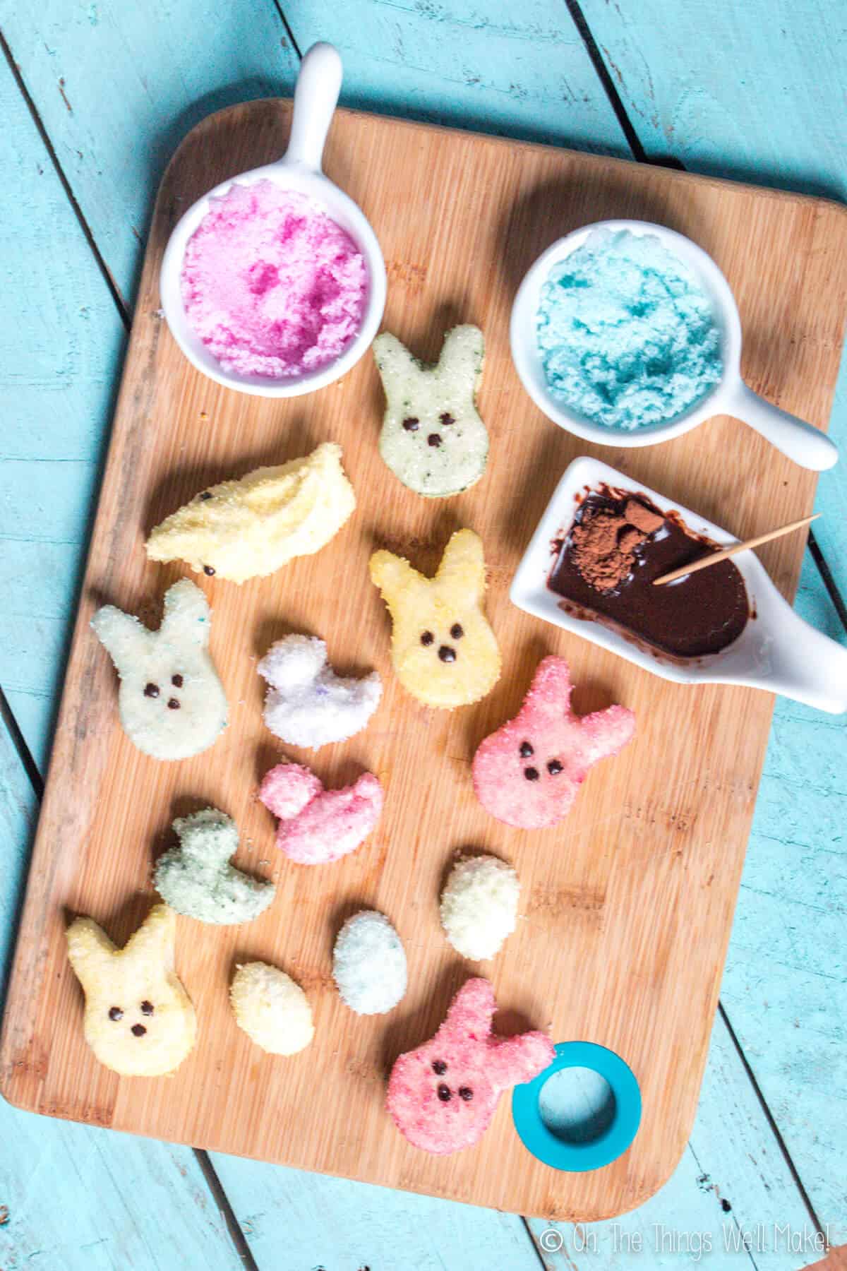 Overhead view of homemade marshmallow peeps covered with naturally colored sugar crystals on a bamboo cutting board.