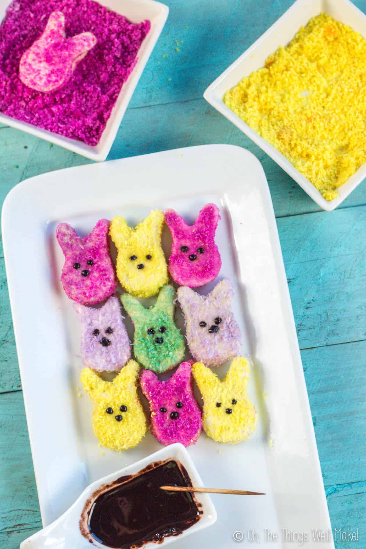 Homemade marshmallow peeps as seen from above on a white plate, along with some chocolate in a small scoop with a toothpick, ready to add chocolate eyes and nose to the peeps.