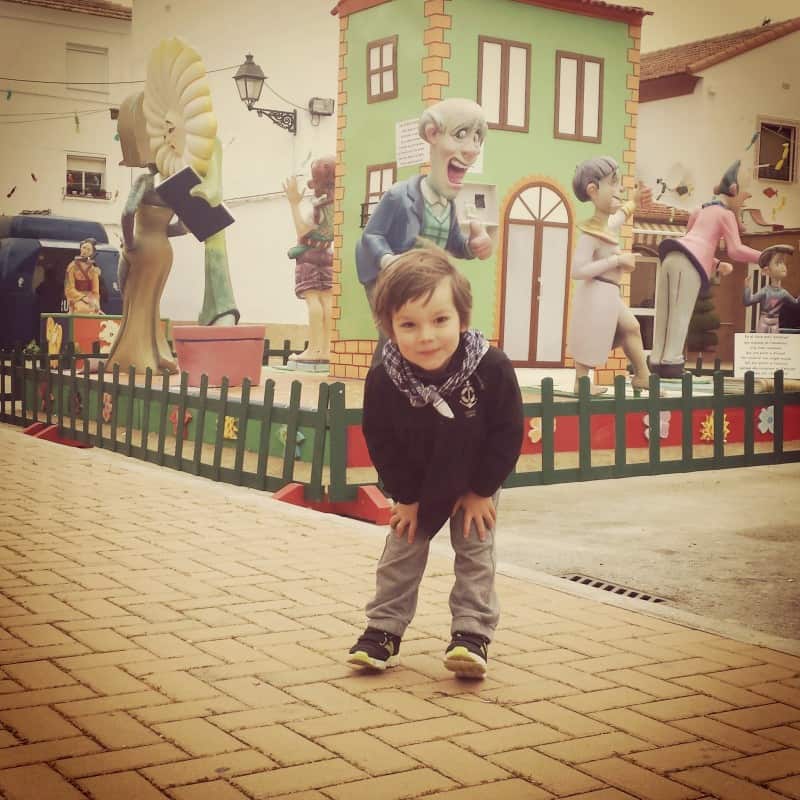 A little boy dressed in a fallero "blusón" in front of a falla.