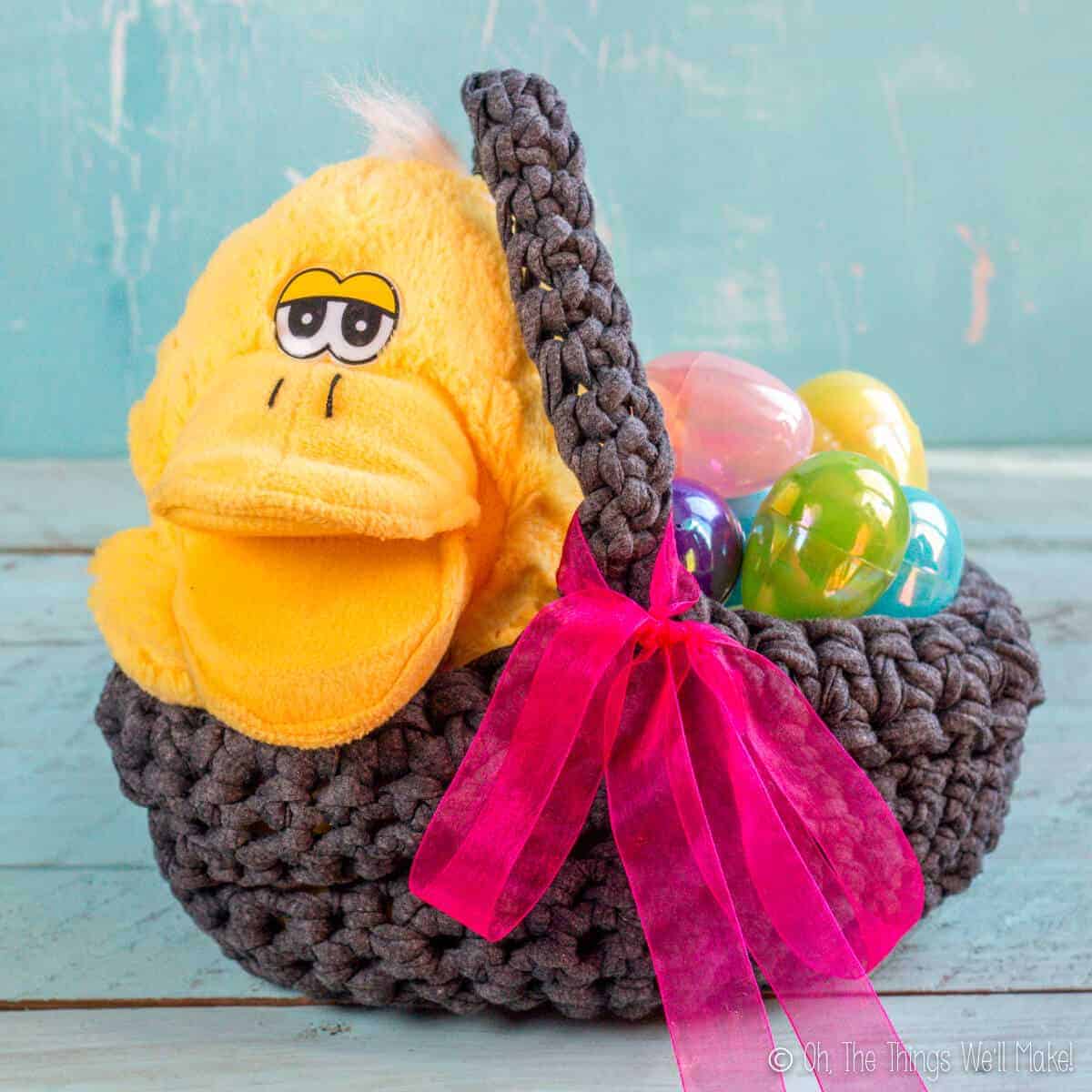 A yellow duck stuffed animal and plastic eggs inside a homemade Easter basket made from t-shirt scraps. The basket is decorated with a big pink bow.