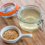 Overhead view of a jar full of homemade hair gel made out of flaxseed next to a spoonful of flaxseeds