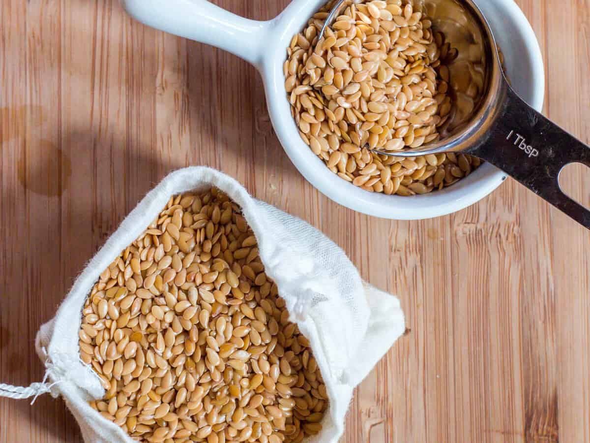 Overhead view of some golden flaxseeds in a cotton pouch and in a bowl with a tablespoon in it.