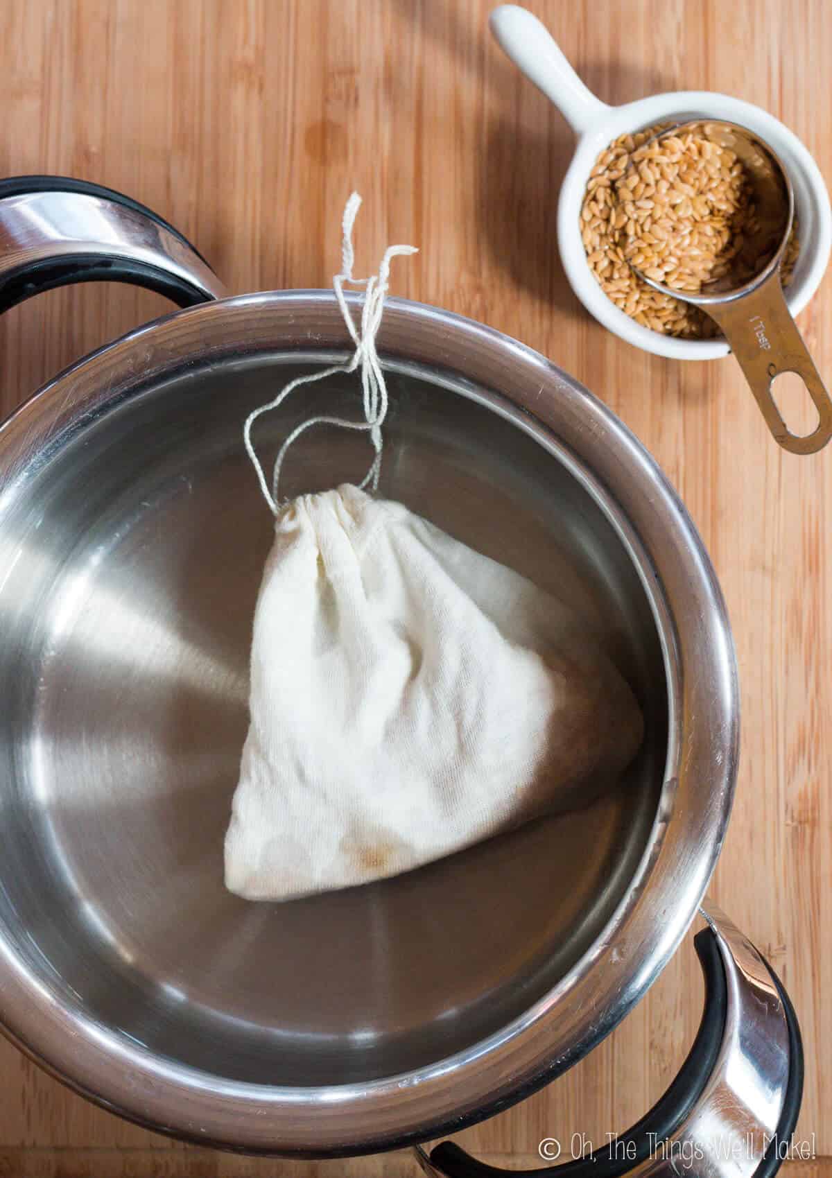 A cotton bag filled with flaxseeds in a pot of water. Next to the pot is a small bowl of flaxseeds.