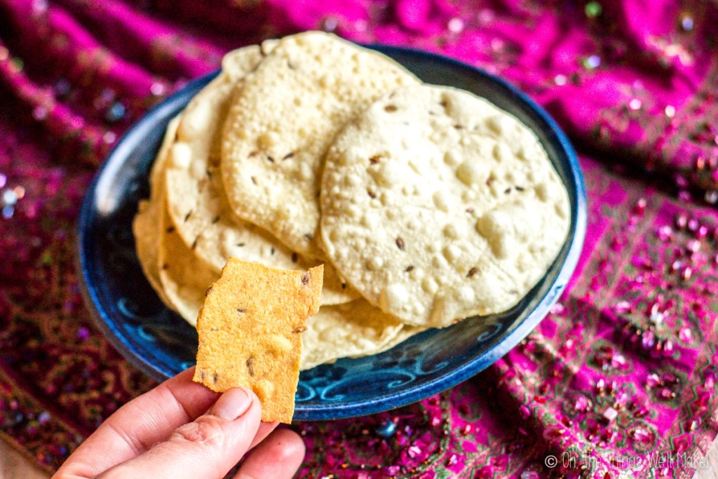 A piece of a lentil cracker in front of a bowl of homemade papadums