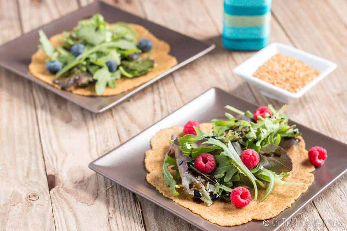 2 flaxseed tortillas on plates covered with lettuce and berries