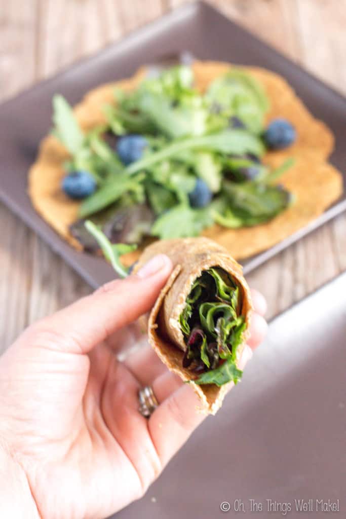 A salad wrapped in a flaxseed tortilla in front of with another tortilla and more lettuce on it.