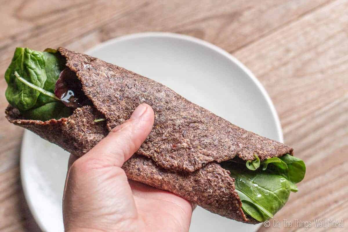 vegan paleo flaxseed tortilla made with brown flaxseeds shown rolled up around some lettuce.