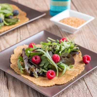 2 flaxseed tortillas on plates covered with lettuce and berries