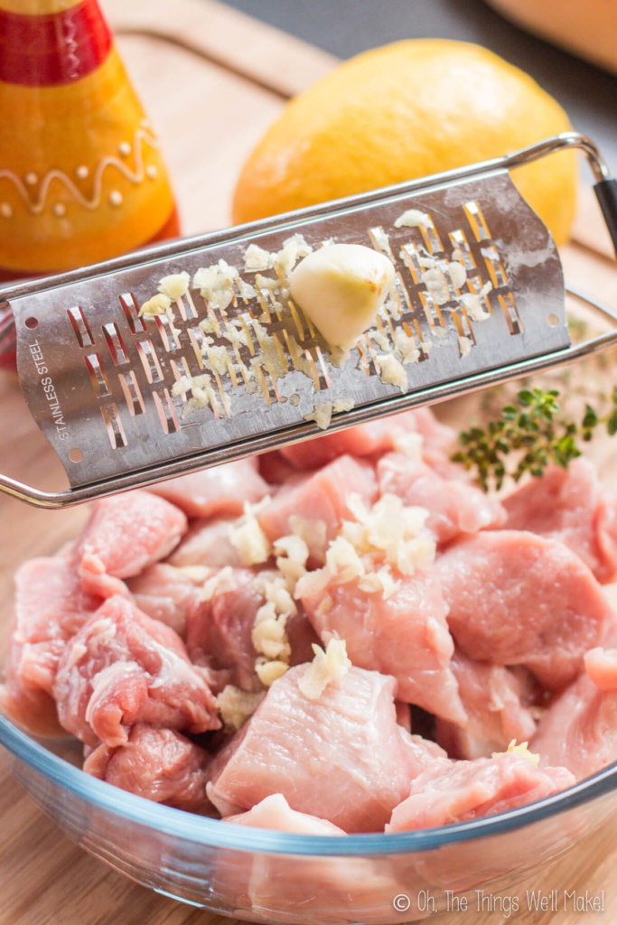 grating garlic over cubes of pork in a glass bowl