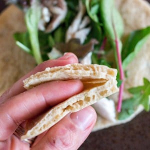 Close-up overhead view of a hand holding a homemade paleo pita bread folded in half with a pita bread full of leafy greens in the background.