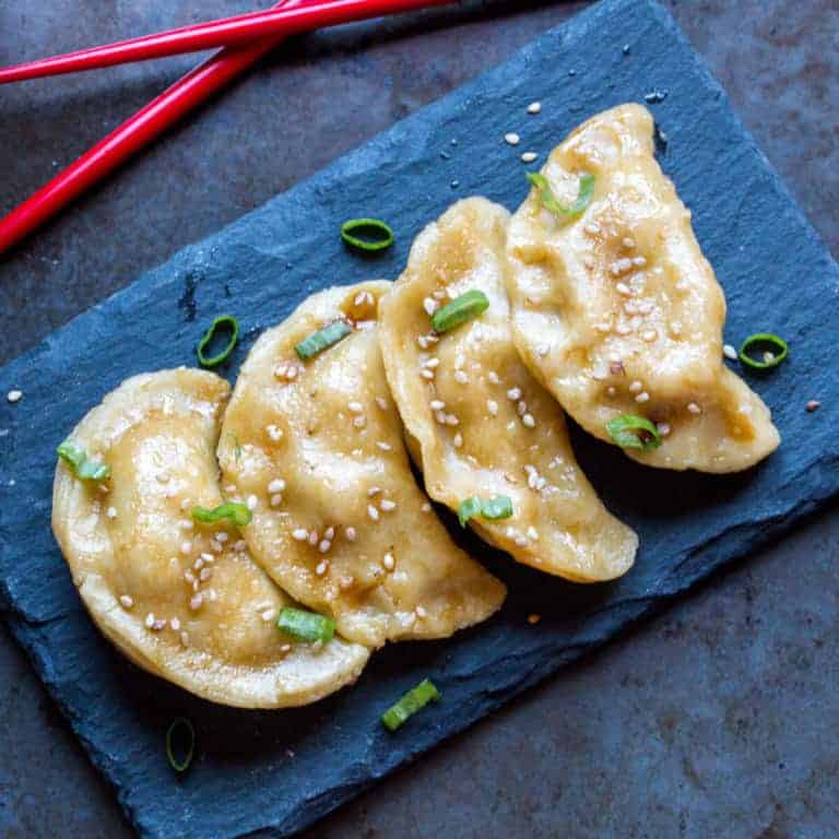 Overhead view of 4 pieces of pot stickers made from homemade paleo pasta filled with ginger and pork, placed on a stone black plate.