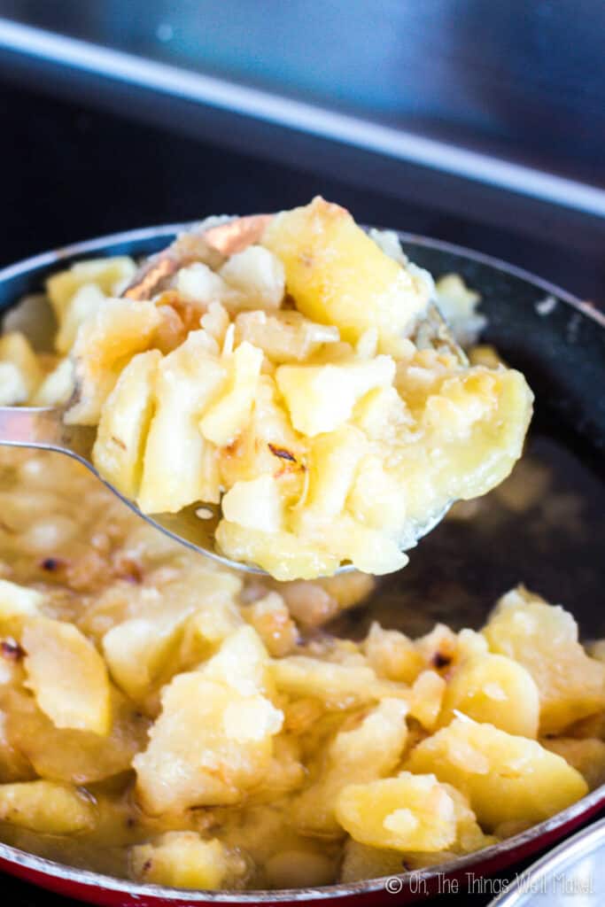 Scooping cooked potatoes out of a frying pan using a large spoon with drainage holes.