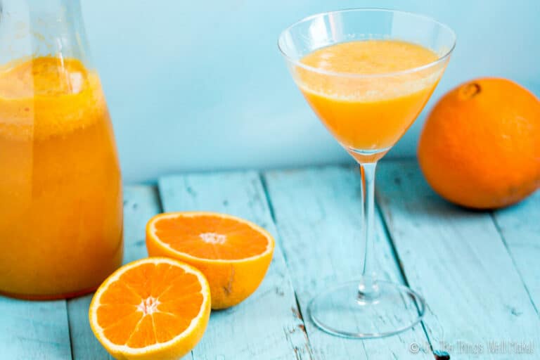 A martini glass filled with agua de Valencia next to a carafe of more of the orange-based cocktail.