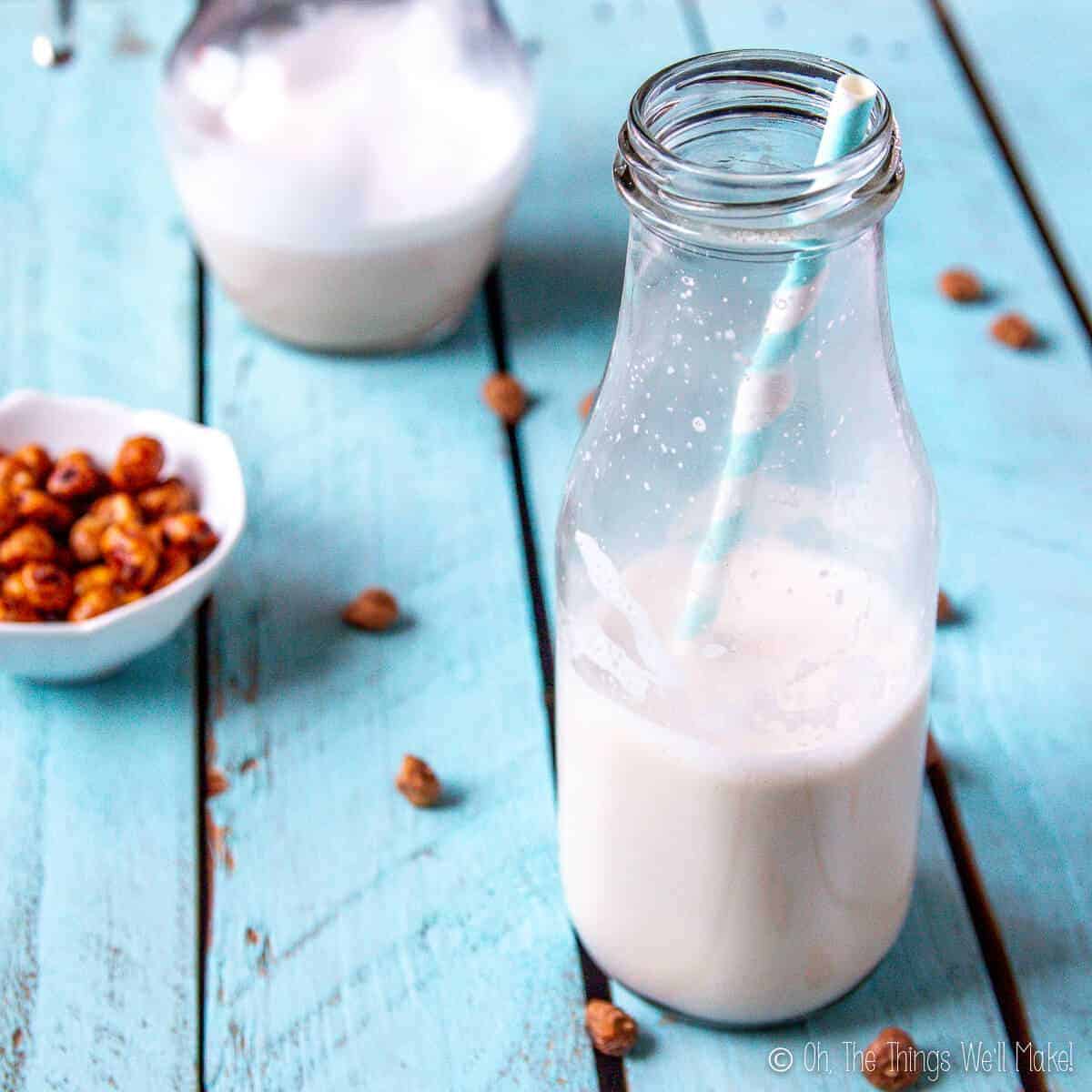 A bottle of tigernut milk (horchata de chufa) in front of a pitcher filled with more tiger nut milk, both surrounded by tiger nuts.