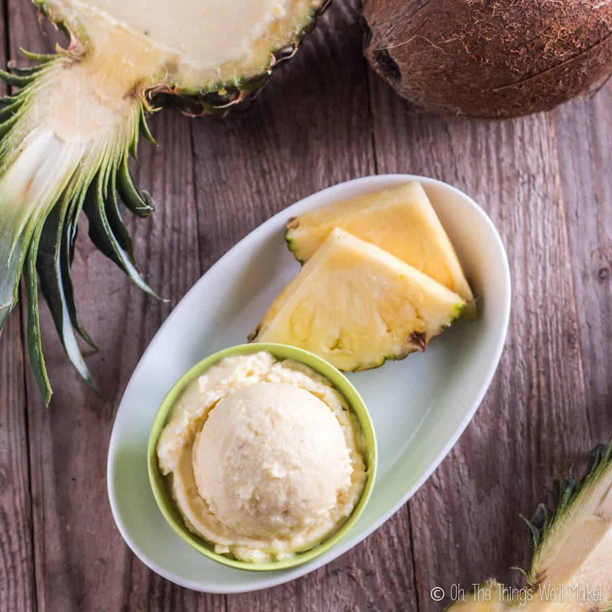 A scoop of pineapple ice cream on a plate with some slices of pineapple.