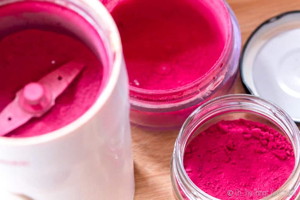 Overhead view of a jar of homemade beetroot powder next to a coffee grinder filled with the ground beetroot.