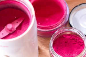 Overhead view of a jar of homemade beetroot powder next to a coffee grinder filled with the ground beetroot.