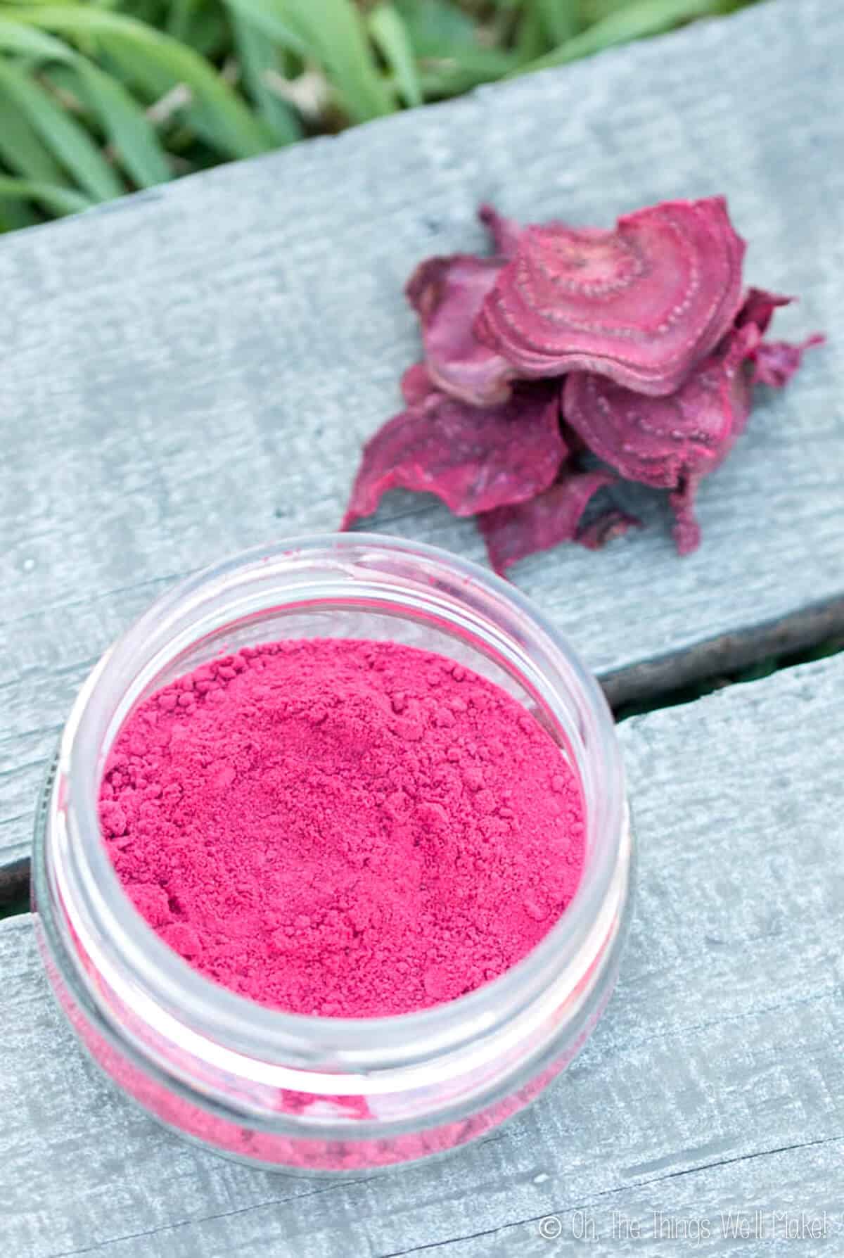 Overhead view of homemade beetroot powder in an open glass jar, next to some dried beetroot slices.