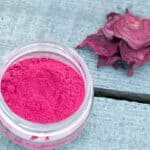 Overhead view of homemade beetroot powder in an open glass jar, next to some dried beetroot slices.