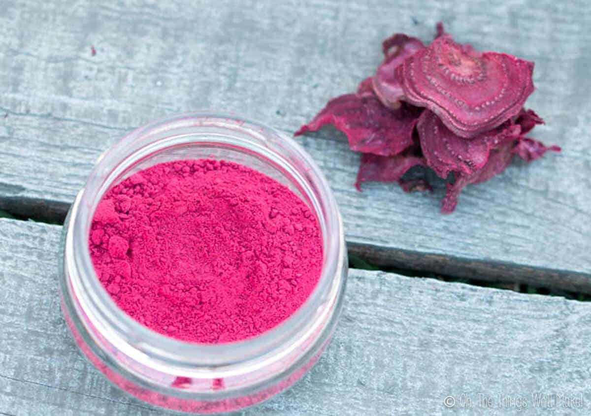 Overhead view of homemade beetroot powder in an open glass jar, next to some dried beetroot slices.