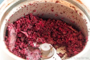 Closeup of the interior of a coffee grinder filled with ground beetroot. It wasn't fully dried, so it clumps together.