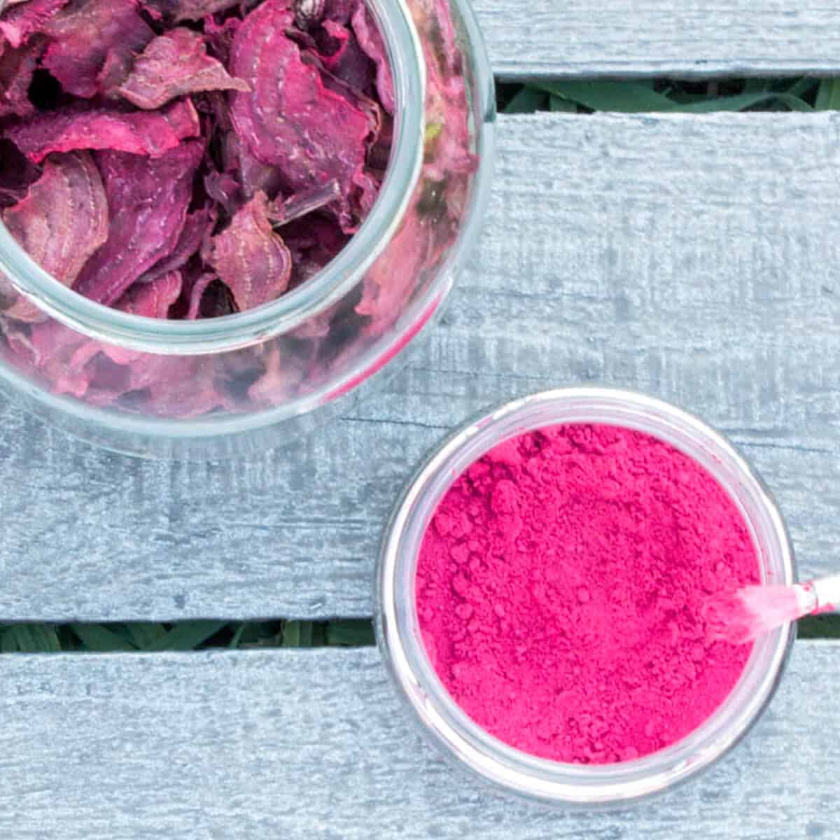 Overhead view of homemade beetroot powder in an open glass jar, next to some dried beetroot slices.