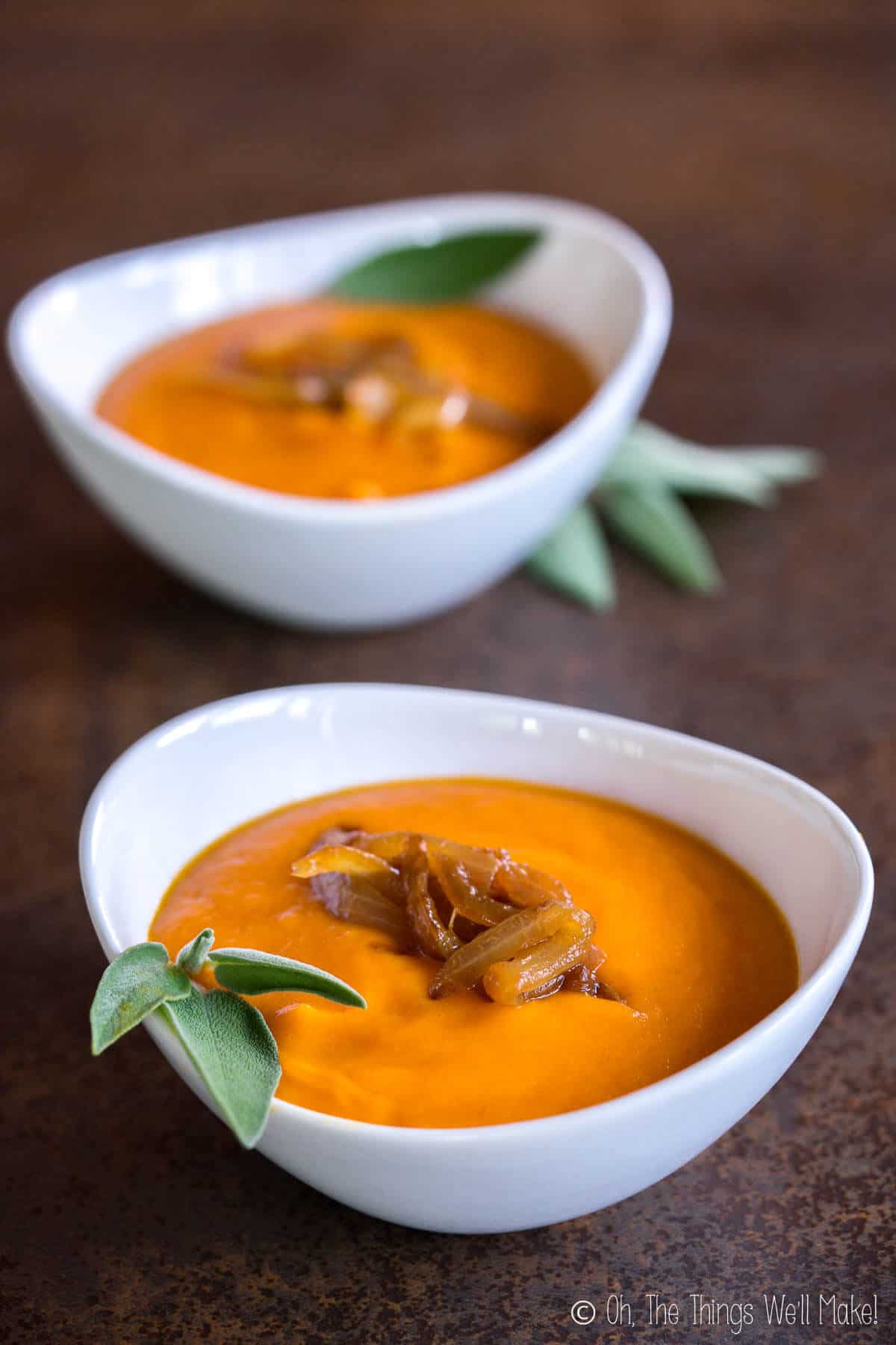 Two bowls of creamy, roasted pumpkin soup garnished with caramelized onions and fresh sage leaves