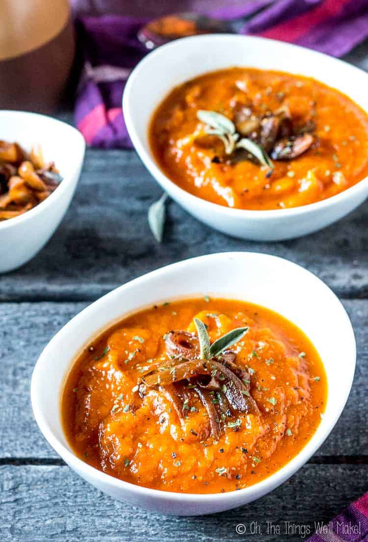 Overhead view of two bowls of a roasted pumpkin and red pepper soup garnished with caramelized onions.