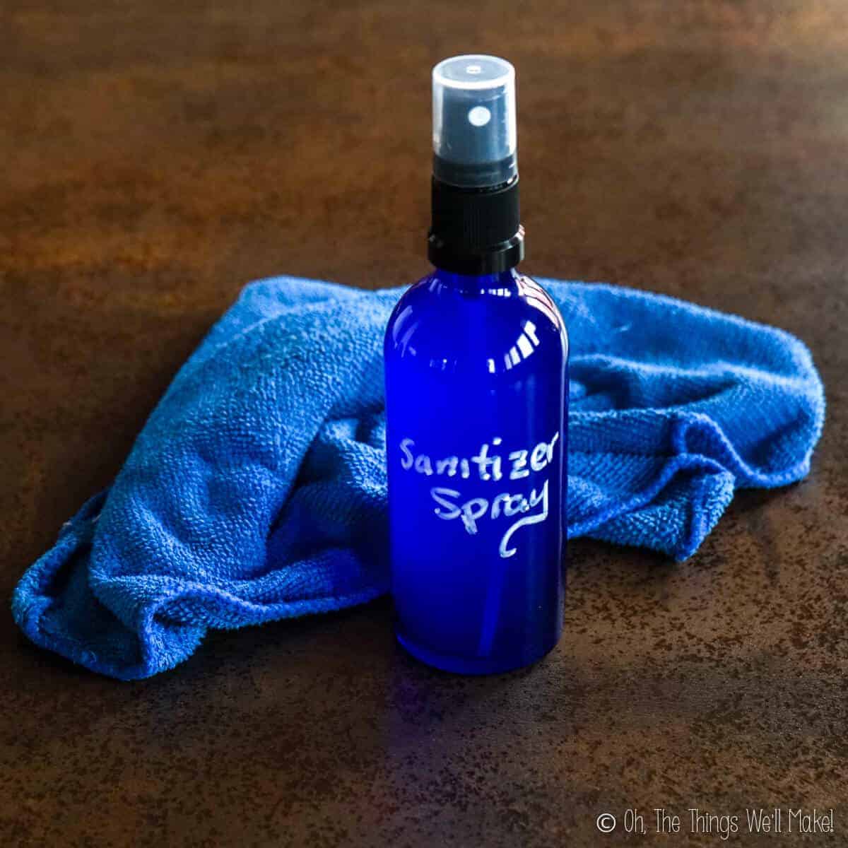 A blue glass bottle filled with a homemade disinfectant spray in front of a blue rag.